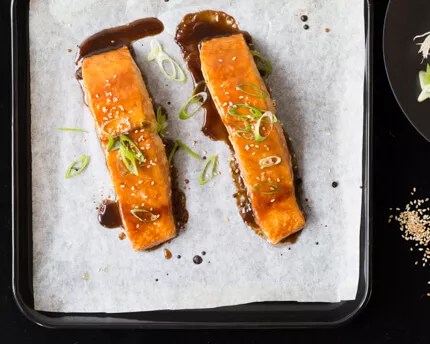 Two pieces of Lacquered Salmon with Crispy Skin on baking sheet with parchment paper