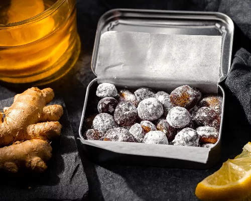 Homemade cough drops in a tin beside lemon slices, ginger root, and honey