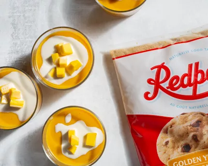 Five glass bowls of mango pudding topped with mango and evaporated milk, and two black spoons