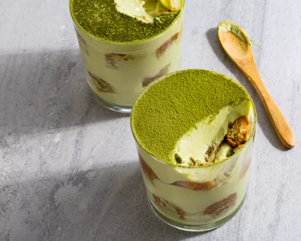 Two glass cups of tiramisu sprinkled with green matcha powder