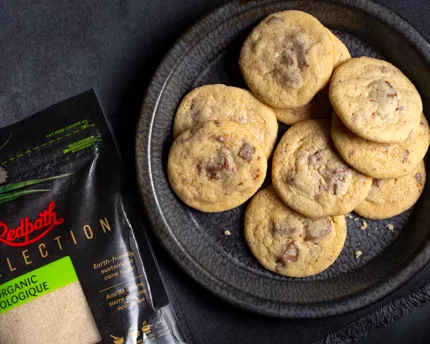 Milk chocolate chunk sugar cookies on a black plate with a black napkin on a black slate counter