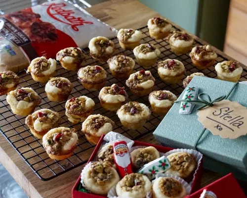 A tray of fruit and nut tarts on grid with cookie boxes