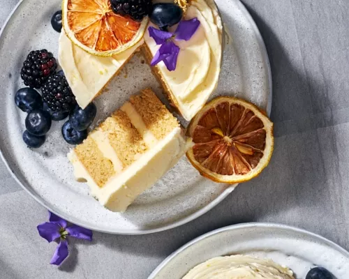 A miniature lemon chamomile cake on a plate with a slice cut, served with berries and topped with berries, edible flower petals,