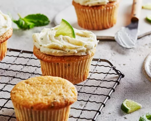 Mojito cupcakes on a wire cooling rack, some topped with ermine frosting and garnished with lime.