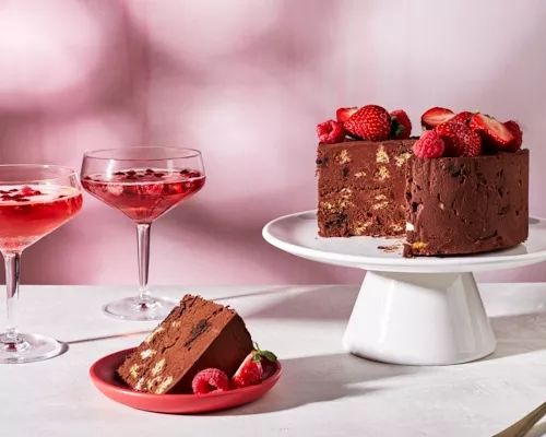 No-bake Mexican Chocolate Wafer Cake topped with strawberries and raspberries on a white cake stand with a piece cut out and se