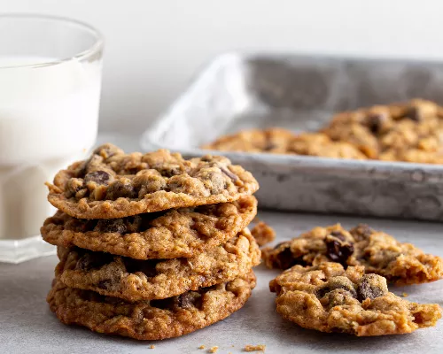 A stack of oatmeal chocolate chip cookies with a glass of milk and a tin serving tray.