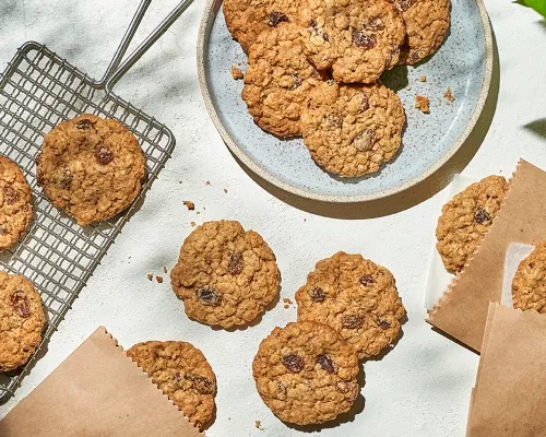 Soft oatmeal raisin cookies on a plate, a cooling rack, a table, and in paper sleeves