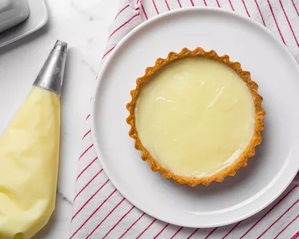 A piping bag beside a tart filled with cream