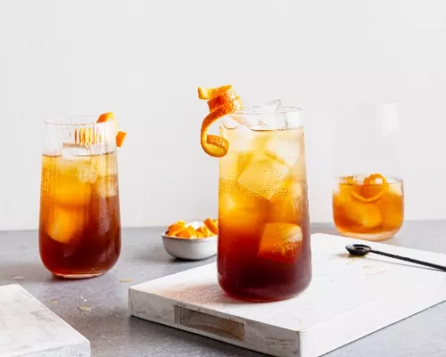 Three glasses of Orange Cold Brew Coffee Spritz with ice and garnished with orange peel.