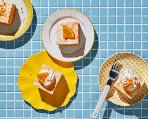 Four pieces of orange vanilla ice cream cake on plates on a blue tiled counter