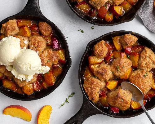 Three peach cobblers served in cast iron frying pans, one with vanilla ice cream