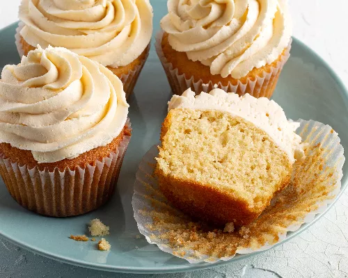 Four iced vanilla cupcakes on a plate, one cut in half