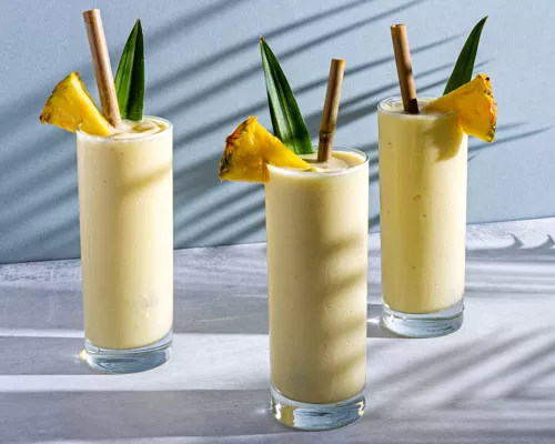 Three glasses of Piña Colada garnished with pineapple spears and leaves, with bamboo straw