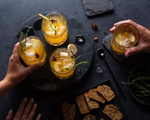 Hands reaching for glasses of Pumpkin Spice rum cocktail, served with crackers