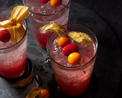 Three glasses of raspberry gooseberry shrub mixed with soda and garnished with raspberries and gooseberrries