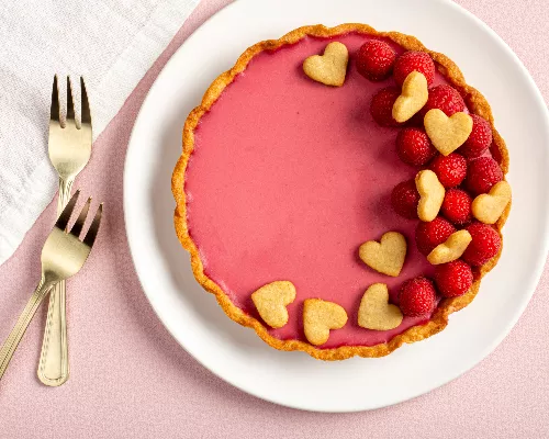 Raspberry rosewater panna cotta tart decorated with raspberries and heart-shaped cookies with 2 golden forks