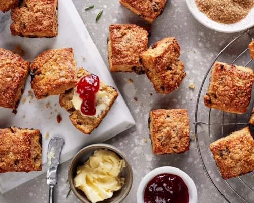 Vanilla rosemary date scones on a platter and a cooling rack shown with dishes of butter and jelly and a bowl of turbinado sugar