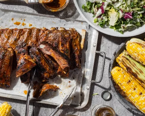 A platter of ribs with mustard barbecue sauce with salad and barbecued corn on the cob