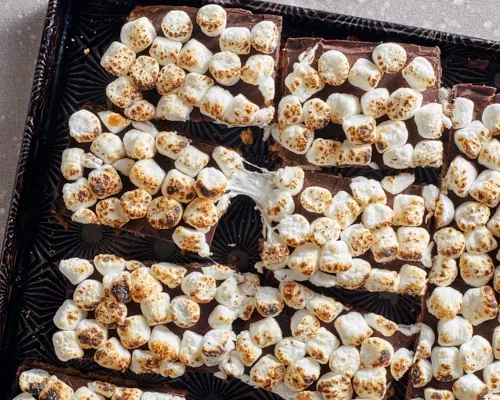 S’mores bars in a black and gold serving tray, with toasted marshmallows partially melted and stretched.