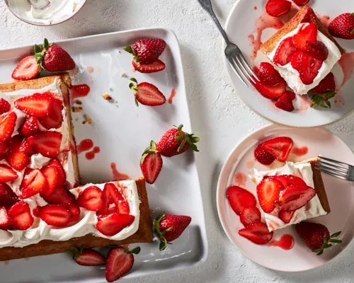 A strawberry-yuzu sheet cake on a white tray served with strawberries, shown with two slices on plates.