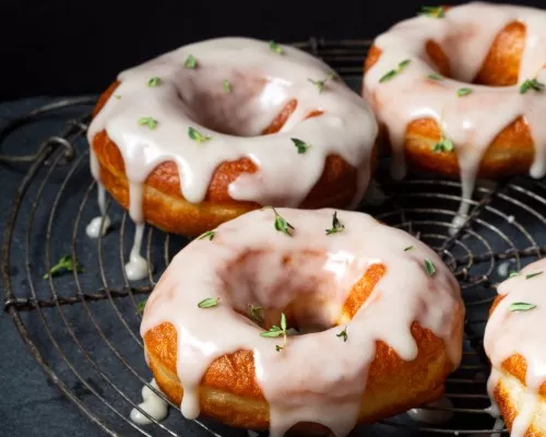 Five yeast donuts on a cooling rack coated with thyme sugar glaze and thyme sprigs