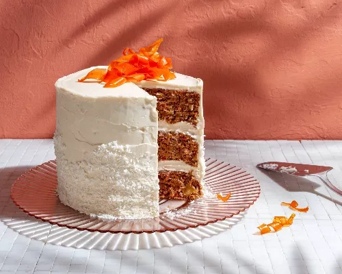 Three-layer vegan carrot cake topped with candied carrot curls on a glass platter