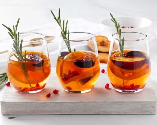 Three glasses of orange sangria with peaches, oranges and herbs in the glasses and background