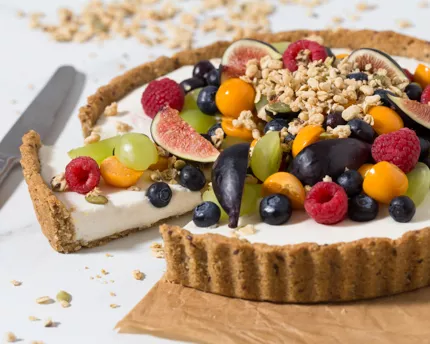 Yogurt Fruit Tart with Granola Crust topped with various fruit and granola sitting on a piece of parchment paper