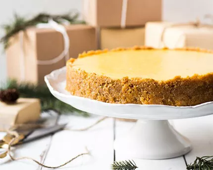 Cheesecake on a cake platter surrounded by presents wrapped in brown paper