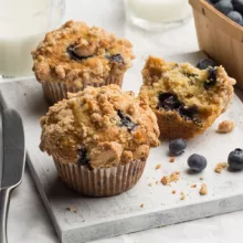 Three blueberry muffins served with milk and a basket of blueberries