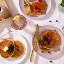 Three plates of easy fluffy pancakes in a picnic setting, with fresh berries, butter and maple syrup