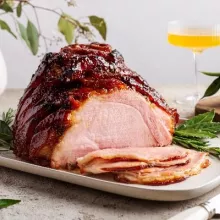 Roasted glazed ham on a platter and garnished with herbs with several slices cut