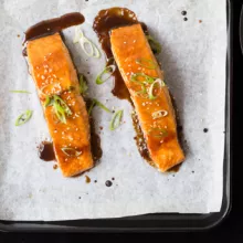 Two pieces of Lacquered Salmon with Crispy Skin on baking sheet with parchment paper