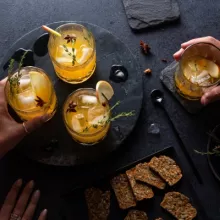 Hands reaching for glasses of Pumpkin Spice rum cocktail, served with crackers