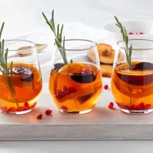 Three glasses of orange sangria with peaches, oranges and herbs in the glasses and background