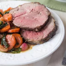 White plate with two slices of mint glazed lamb and candied vegetables