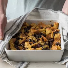 Challah Bread Pudding with Chocolate and Dried Fruit in a serving dish being held with a dish towel