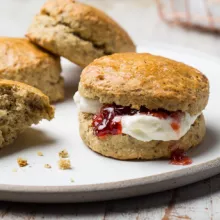 A plate of scones, one with clotted cream and jam