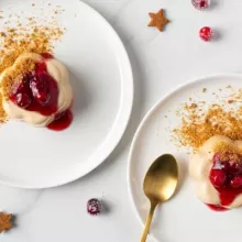 Two gingerbread panna cotta topped with cranberries on white plates with a gold spoon