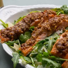 Arugula salad with crusted salmon fillets in a white bowl