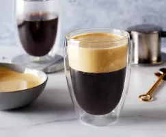 A glass of Vietnamese Egg Foam Coffee shown with a bowl of egg foam, a glass of coffee, and coffee-making equipment.