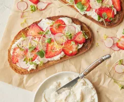 Two slices of toasted bread topped with whipped brown sugar ricotta, sliced strawberries and radishes, and microgreens