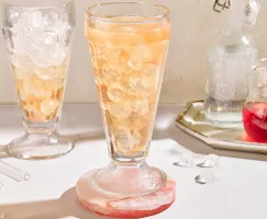 Two parfait glasses of old-fashioned cream soda on ice shown with a bottle of soda and a pitcher of strawberry simple syrup