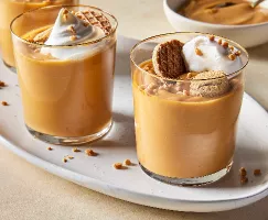 Three glasses of butterscotch pudding on a small oval tray, each topped with whipped cream, toffee bits, and cookies.