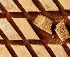 Rows of spiced cake bars cut into diamond shapes, topped with a smooth glaze. One bar is broken in half, revealing a moist and crumbly interior. The warm brown background looks rustic and cozy