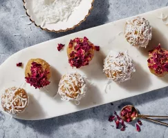 Golden Badam Ladoo garnished with rose petals and coconut on a thin white platter