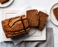Banana bread on a cutting board with pieces cut and slices on plates