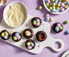 Seven chocolate bird nest cookies topped with white chocolate and candy-coated chocolate eggs on a cutting board