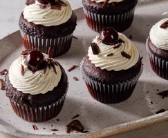 Five Black Forest cupcakes with chantilly icing topped with cherries and shaved chocolate on a platter.