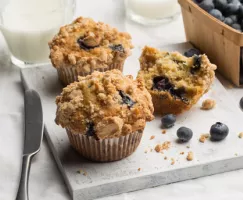 Three blueberry muffins served with milk and a basket of blueberries